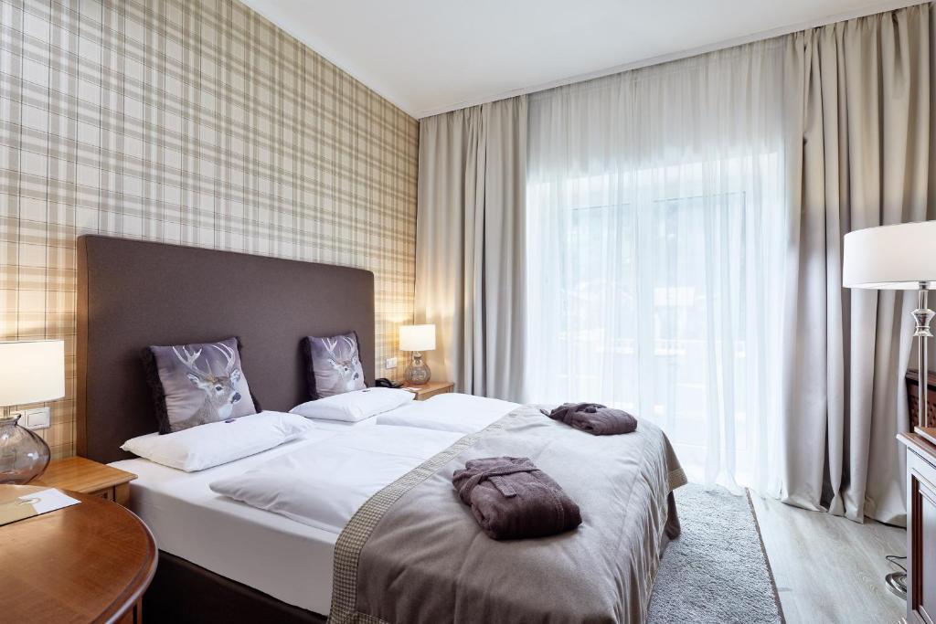 Mūsdienīga guļamistaba ar divguļamo gultu, dekorēta ar stilīgām spilveniem un siltām toņām. Lielie logi nodrošina dabisko apgaismojumu, radot mājīgu atmosfēru.