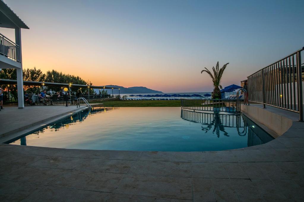 Mūsdienīgs baseins ar skatu uz saulrietu un jūru, apņemts ar zaļu zāli un ērtām atpūtas zonām. Ideāla vieta relaksācijai un atpūtai.