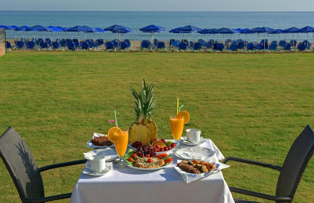 Brokastis ar augļiem un dzērieniem pie jūras, fons ar zilu saules aizsargu krēslām un mierīgu ūdeni.