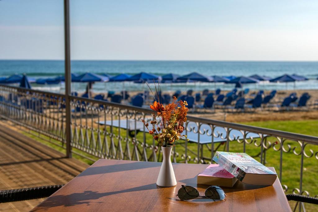 Vasaras brīvdienu atmosfēra ar ziedu pušķi un grāmatu uz galda, skats uz pludmali un jūru, saules gultas fona.