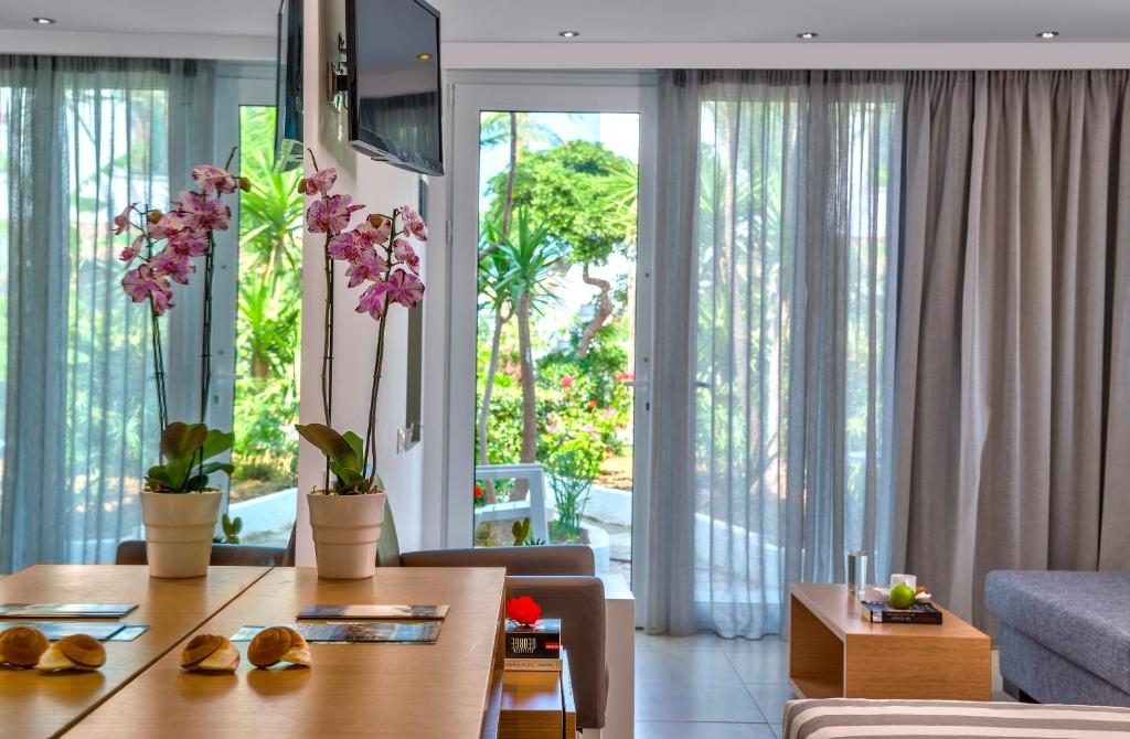 Mūsdienīga viesnīcas numura iekārtojums ar orhidejām uz galda un skatu uz dārzu. Gaisma plūst caur caurspīdīgām aizkariem, radot relaksējošu atmosfēru.