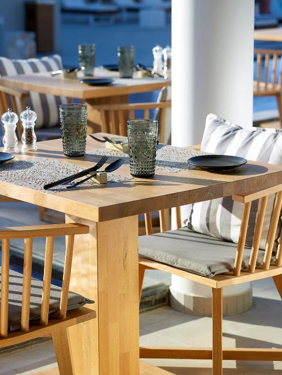 Moderns restorāna galds ar koka kājām, dekorēts ar elegantiem traukiem un stikla glāzēm, piedāvā relaksējošu ēdināšanas pieredzi. Galds ir izvietots ārā, radot patīkamu atmosfēru.