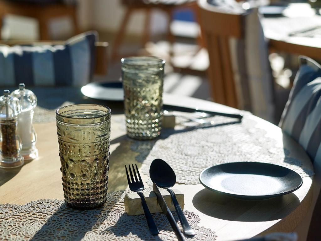 Galda uzstādījums ar dekoratīvām glāzēm, galda piederumiem un porcelāna šķīvi, radot mājīgu atmosfēru. Ideāli piemērots restorāna vai kafijas veikala interjeram.