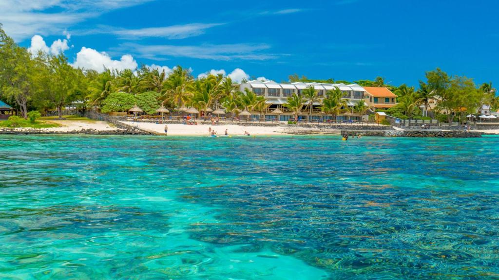 Skaista pludmale ar skaidru ūdeni un palmām, fons ar viesnīcu un zaļām ainavām.