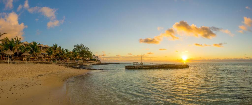 Saulriets pār pludmali ar palmu kokiem un laivām ūdenī, radot mierīgu un gleznainu ainavu. Ideāla vieta atpūtai un relaksācijai.