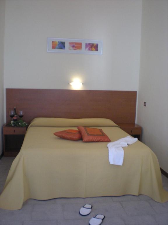 Miega istaba ar dzeltenu gultas veļu un spilveniem, kas rotāti ar oranžiem akcentiem. Uz naktsgaldiņa ir divi vīna glāzes un neliela zaļumu kompozīcija, radot mājīgu atmosfēru.