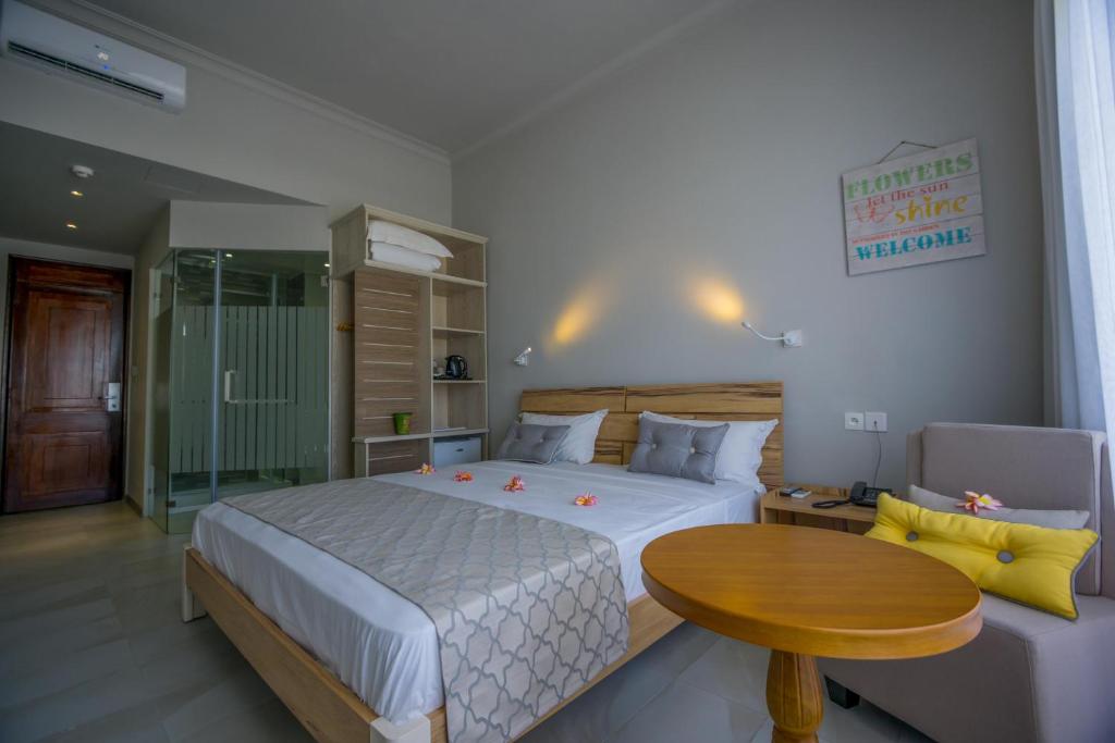 Mūsdienīga viesnīcas numura iekārtojums ar gultu, koka galdu un ērtu krēslu. Telpā ir liels logs, kas nodrošina dabisko apgaismojumu, un vannas istaba ar stikla durvīm.