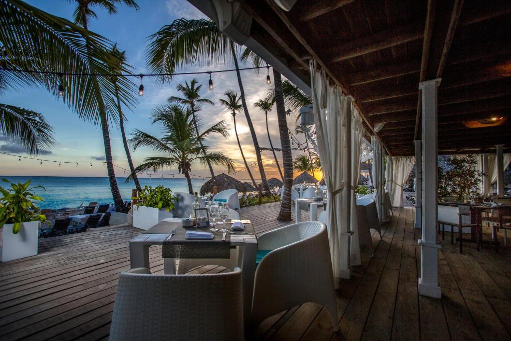 Tropu restorāns ar skatu uz jūru, kur vakara gaismā redzami palmas un romantiska atmosfēra. Ideāla vieta relaksācijai un baudīšanai.
