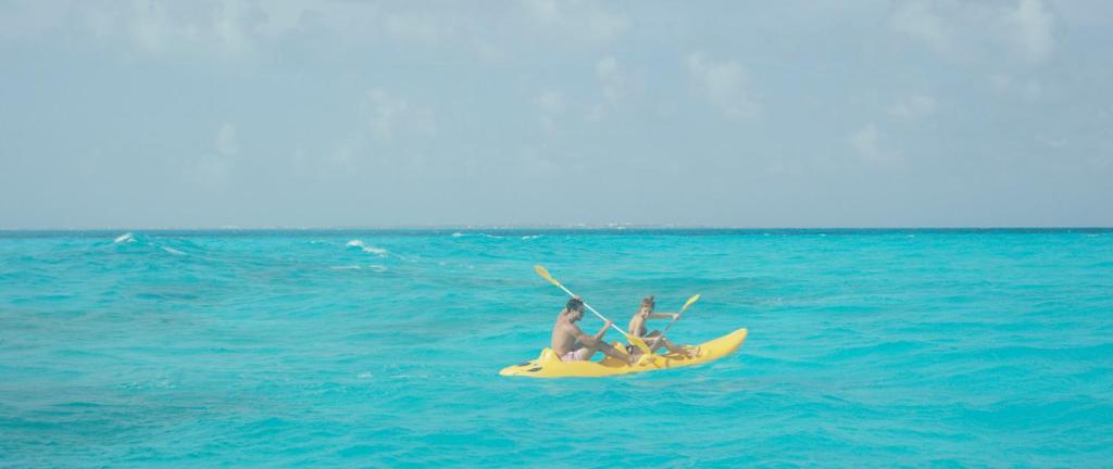 Divi cilvēki airē dzeltenā kajakā, izpētot kristāldzidru okeānu ar gaiši zilu ūdeni. Ideāla vasaras aktivitāte saulainā dienā.