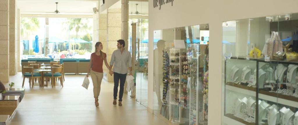 Pāris, turēdams iepirkšanās somas, pastaigājas pa modernu iepirkšanās centru ar rotaslietām un kafijas vietām. Gaisīga un eleganta vide veicina relaksējošu atmosfēru.