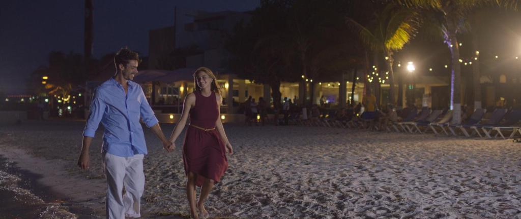 Jauna pāra romantiska pastaiga pa pludmali naktī, apgaismojums un palmām apkārt. Pārsteidzoša atmosfēra un brīnišķīgas atmiņas.