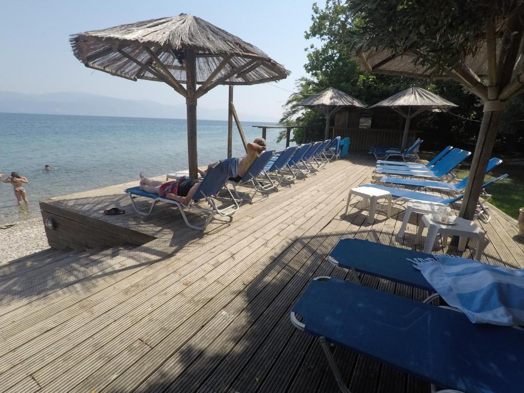 Pludmales atpūtas zona ar sauļošanās krēsliem un lietussargiem, blakus skaidram ūdenim un pludmales smiltīm. Ideāla vieta relaksācijai un peldēšanai.