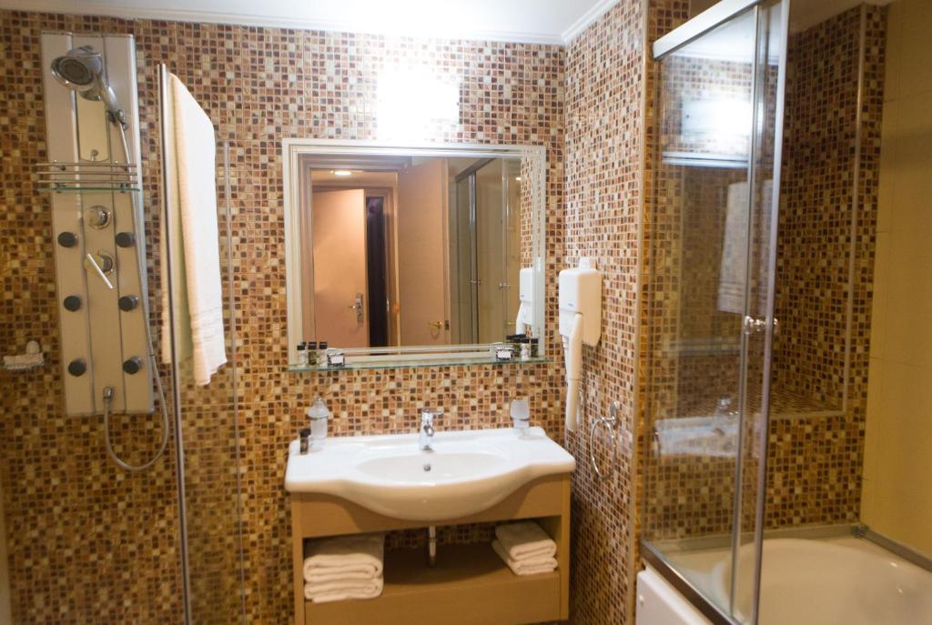 Mūsdienīgs vannas istabas interjers ar mozaīkas flīzēm, dušas kabīni un izlietni, kas papildināta ar higiēnas piederumiem. Elegants un funkcionāls dizains.