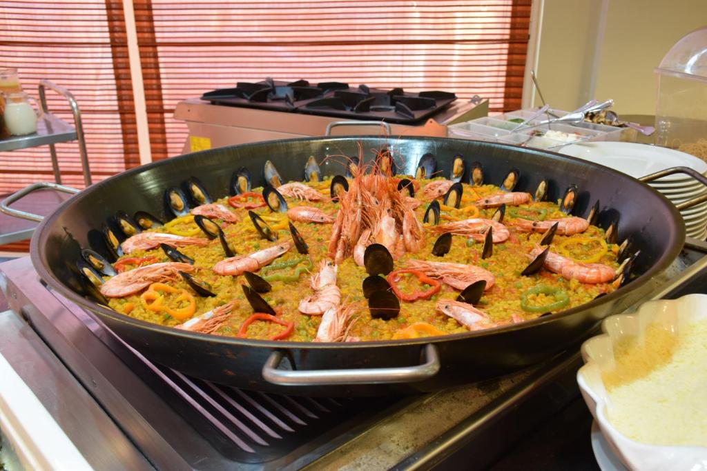 Lielā panna ar garšīgiem jūras produktiem, ieskaitot garneles un gliemenes, apzeltīta ar dažādām dārzeņu šķēlītēm. Panna tiek pasniegta uz virtuves galda, radot apetīti veidojošu skatu.