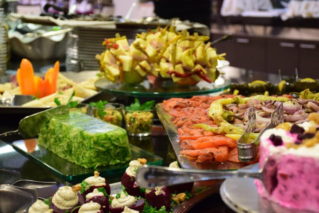 Dažādu ēdienu bufete ar krāsainām uzkodām, dārzeņiem un desertiem, kas sakārtoti uz galda. Iekļauti svaigi augļi, zivis un dzīvnieku izcelsmes produkti.