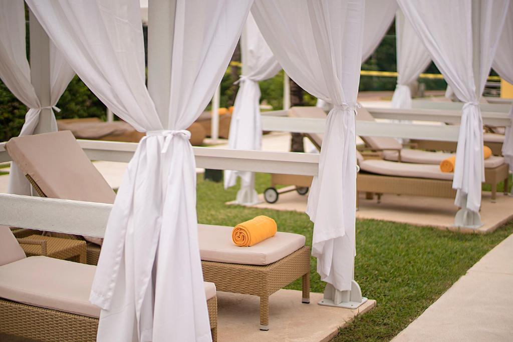 Relaksējošs atpūtas stūris pie JOIA Paraiso by Iberostar ar gultām un baltām aizkariem.