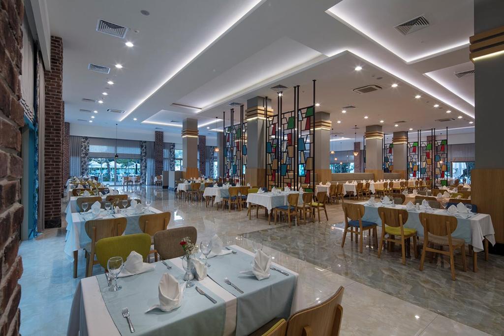 Mūsdienīgs restorāns ar elegantiem galdiem un krāsainiem logu elementiem, Dosinia Luxury Resort.
