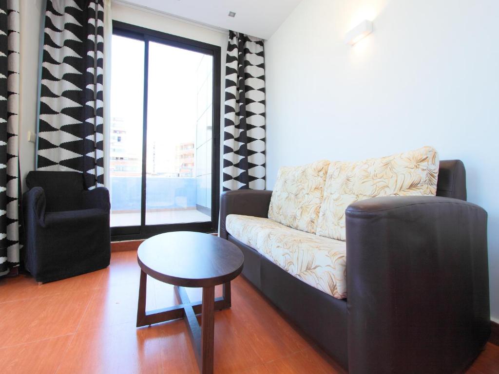 Mūsdienīgs viesistabas interjers ar dīvānu un krēslu, kas izceļas ar melnbaltām aizkariem un lieliem logiem, kas nodrošina dabisko apgaismojumu.