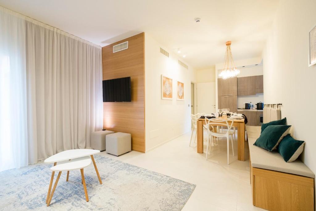 Mūsdienīgs viesistabas interjers ar koka akcentiem, ērtu dīvānu un ēdamgaldu, kas izveidots gaisīgā un gaišā vidē. Sienas rotā mākslas darbi, un telpa ir aprīkota ar televizoru un virtuves stūri.