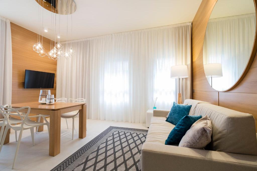 Mūsdienīgs viesistabas interjers ar koka akcentiem, gaismas ķermeni un plašu logu, kas ļauj ienākt dabiskajai gaismai. Stils ir minimālistisks ar ērtu dīvānu un elegantiem galda krēsliem.