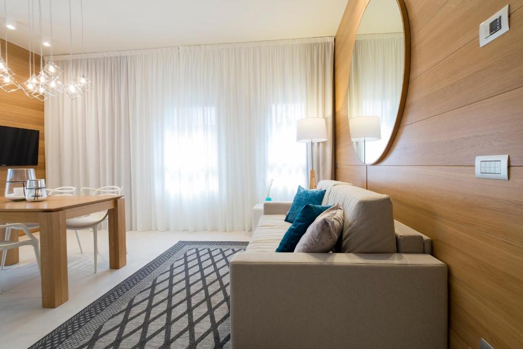 Mūsdienīgs viesistabas interjers ar gaišām krāsām, koka apdari un elegantu apgaismojumu. Sēdvietas ar spilveniem un liels spogulis pie sienas.