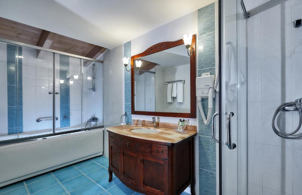 Mūsdienīgs vannas istabas interjers ar koka griestiem, akmens izskata izlietni un stikla dušu. Eleganta vannas istaba ar gaišiem flīzēm un tradicionālu mēbeļu dizainu.