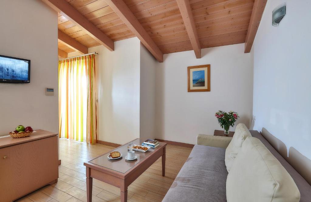 Gaiša un mājīga viesistaba ar koka griestiem, televizoru un logu ar krāsainām aizkariem. Uz galda atrodas kafija un uzkodas, radot patīkamu atmosfēru.