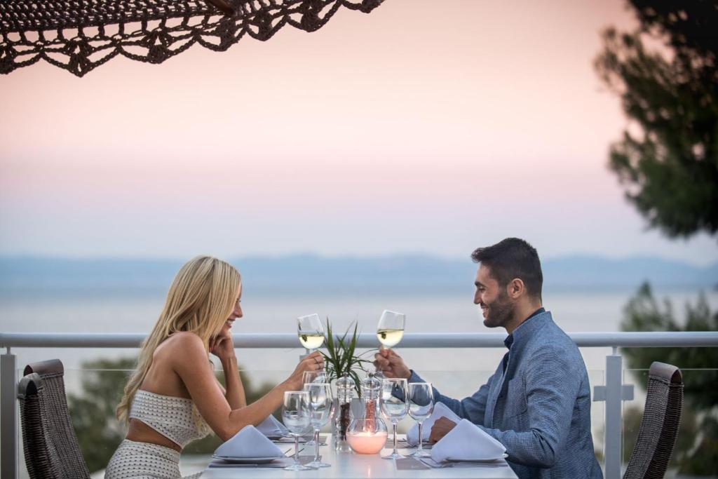 Romantiska vakariņas pāri pie galda ar vīnu, fona ainava un saulriets. Ideāla atmosfēra īpašiem mirkļiem.