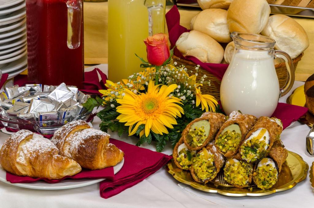 Bagātīgs brokastu galds ar kruasāniem, saldētiem desertiem, pienu un sulām, rotāts ar ziediem.