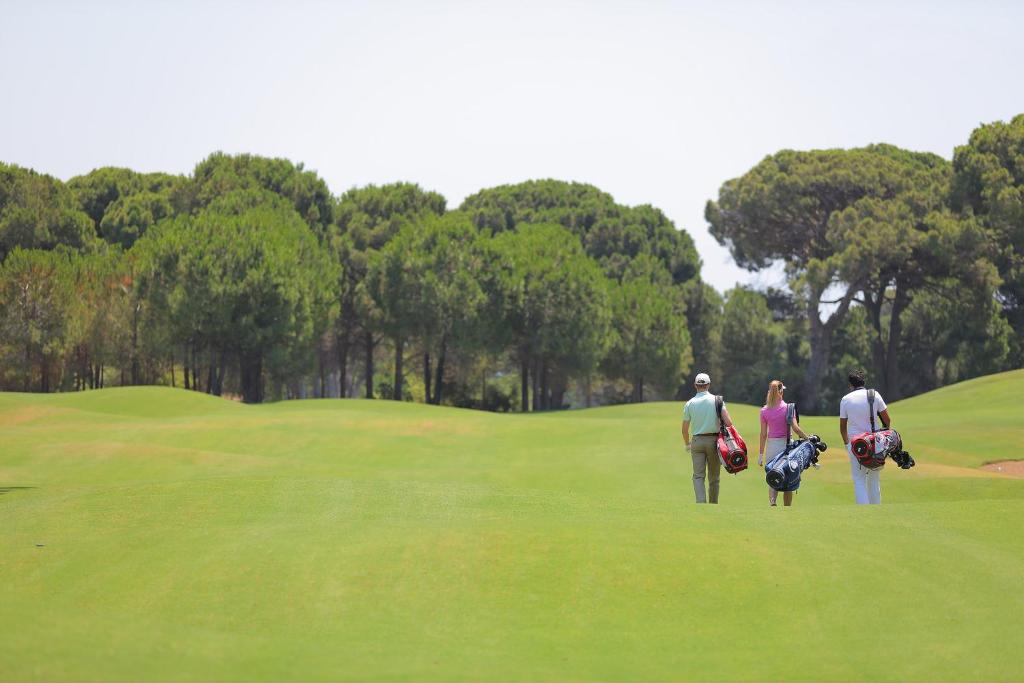Trīs golfa spēlētāji, dodoties uz zaļo laukumu Sueno Hotels Golf Belek.