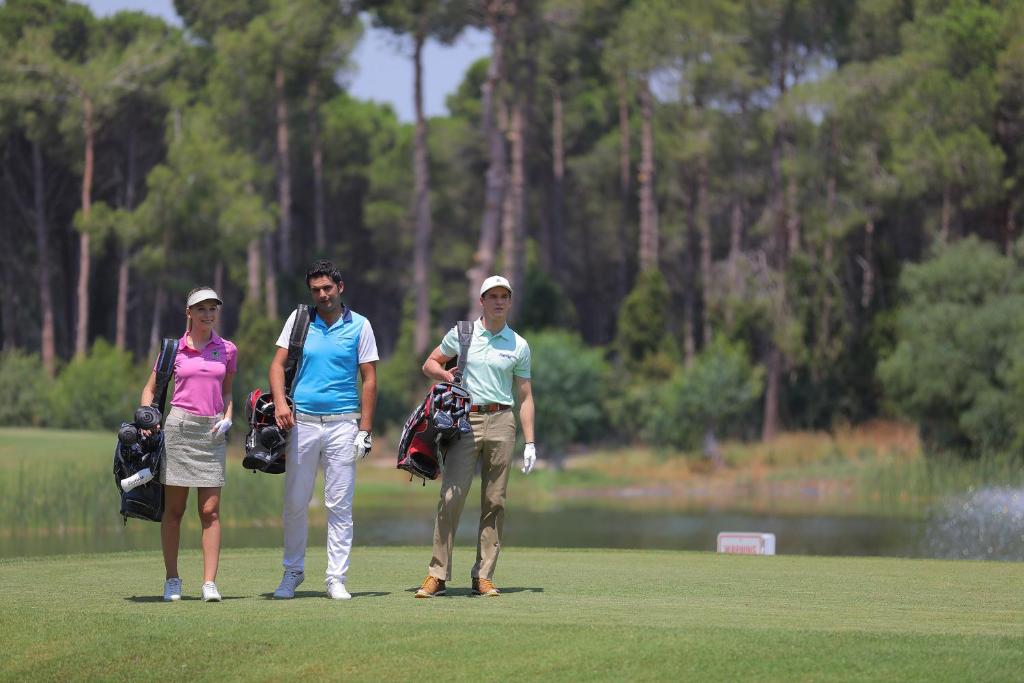 Trīs golfa spēlētāji, dodoties pa zaļu lauku Sueno Hotels Golf Belek.