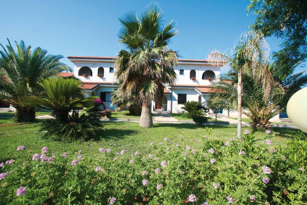 Viesnīca ar tropiskiem augiem un ziediem, kas ieskauj ēku ar sarkanu jumtu, saulainā laika apstākļos.