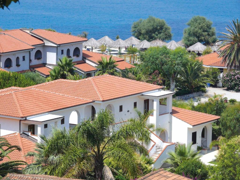 Piekrasna kūrorta ainava ar baltiem māju jumtiem un ziedošiem dārziem, kas atrodas pie zila jūras ūdens.