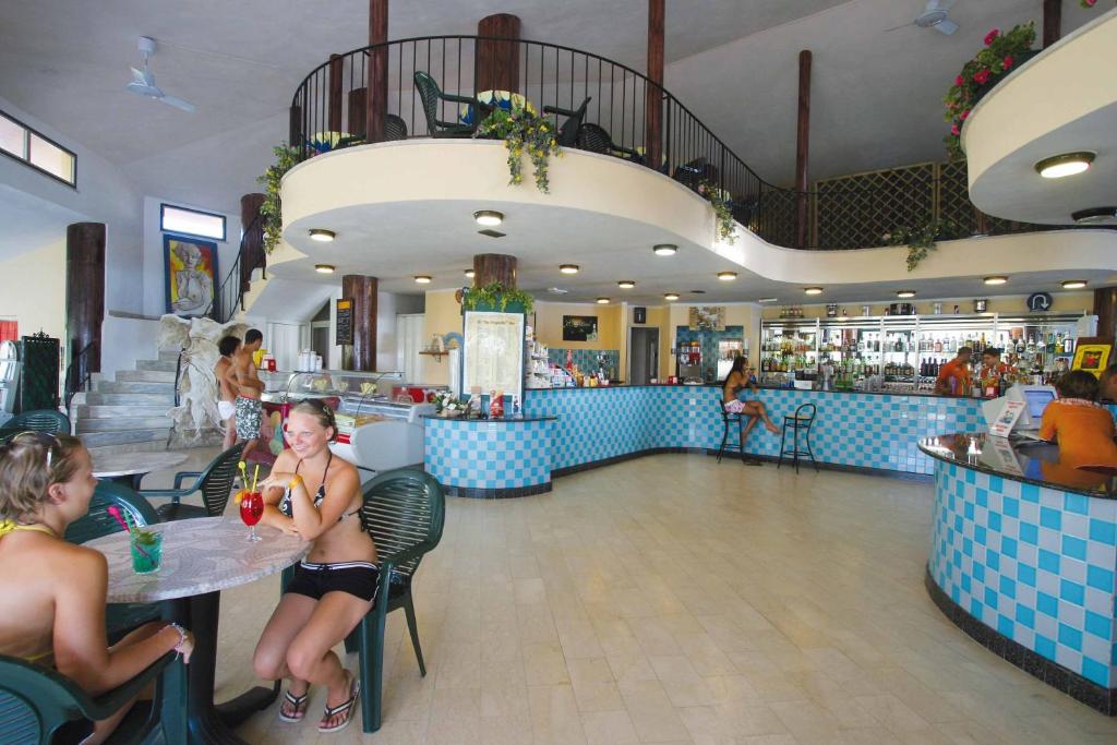 Viesnīcas bārs ar modernu interjeru, kurā viesi bauda dzērienus un relaksējas pie galdiem. Redzami vairāki cilvēki, kas izbauda atpūtu un socializēšanu.