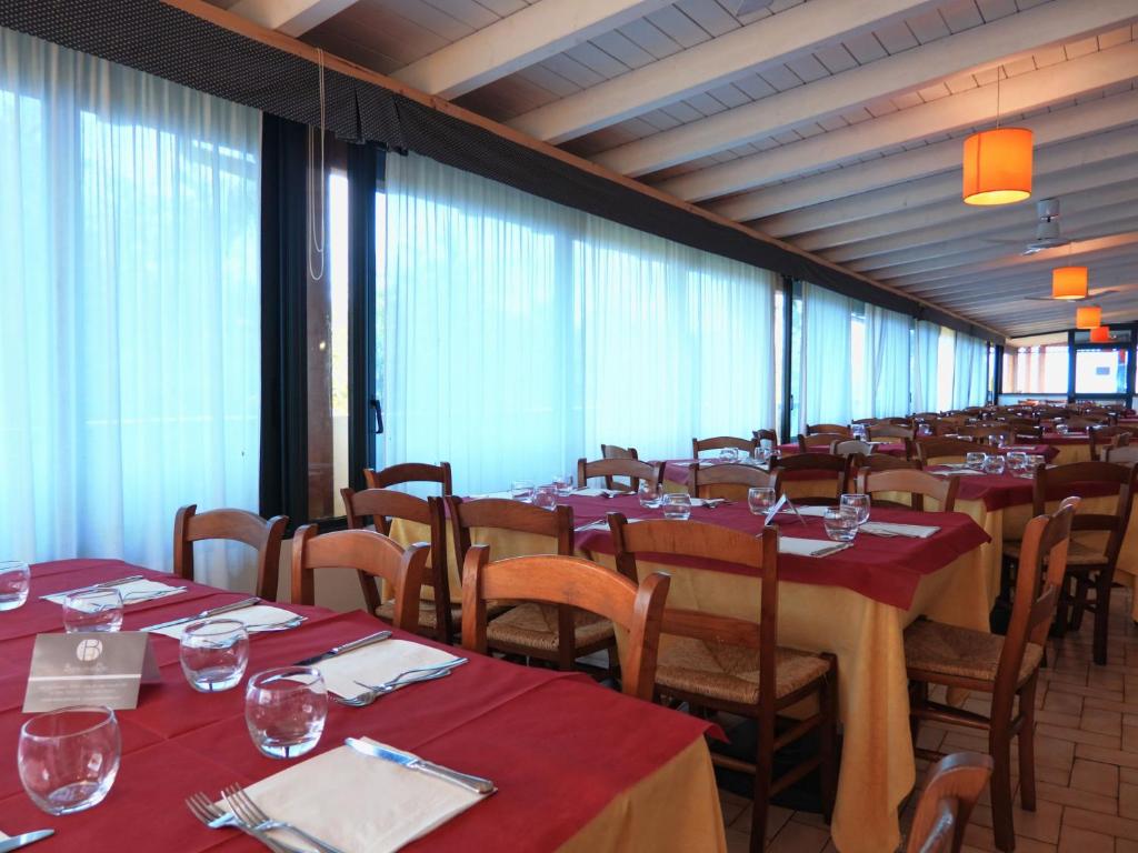 Gaišs restorāna interjers ar koka galdiem un sarkaniem galdautiem, apgaismots ar oranžām lampām. Lielas logu ailes ar caurspīdīgām aizkariem, radot viesmīlīgu atmosfēru.