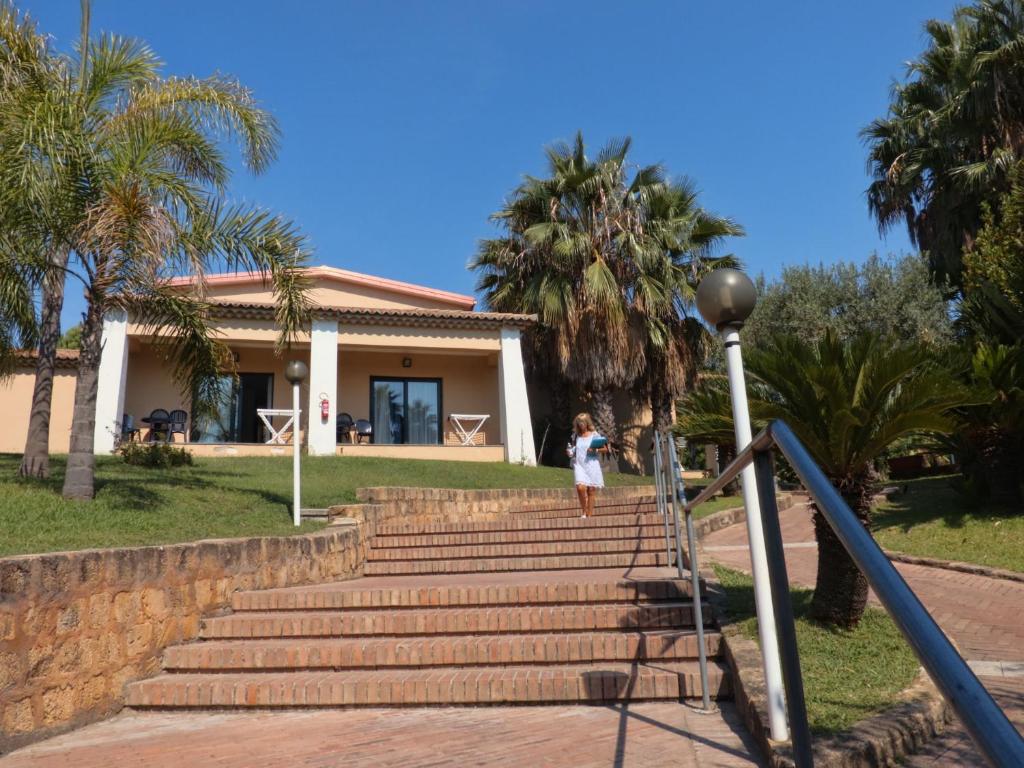 Vasaras māja ar palmas kokiem un saulainu zilo debesu fonu, sieviete kāpj pa akmens kāpnēm.