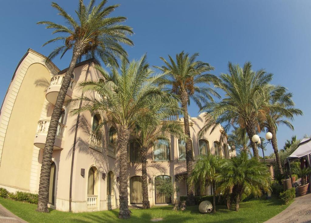 Elegantā villa ar palmu kokiem un saulainu debesu fonu, radot tropisku atmosfēru. Ideāli piemērota atpūtai un brīvdienām.