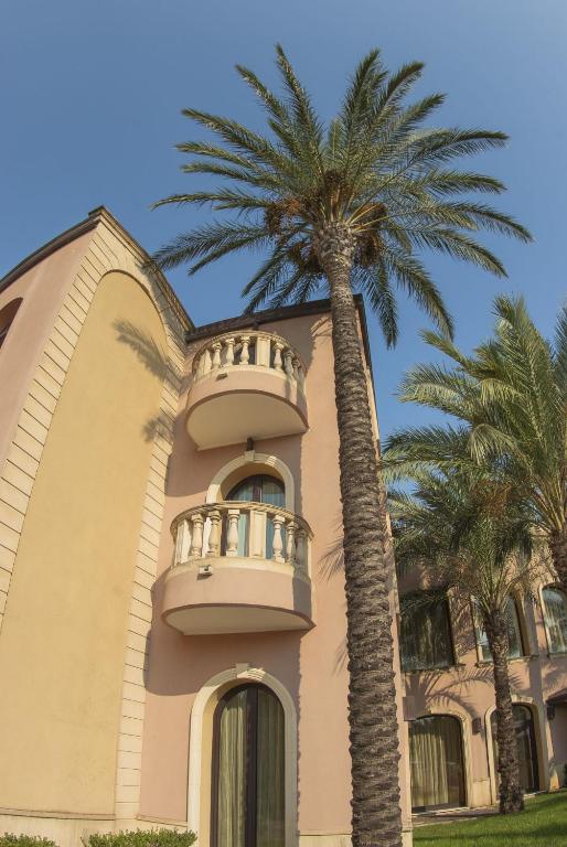 Elegantā ēka ar balto balkonu un palmu ainavu, radot tropisku atmosfēru. Ideāls brīvdienu galamērķis pie jūras.