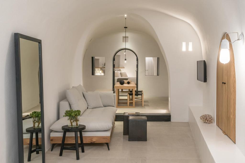 Mūsdienīga viesistaba ar arku veidotām sienām, pelēku dīvānu un koka mēbelēm, kas rada siltu un mājīgu atmosfēru. Telpa ir gaiša ar minimālisma dizainu un dabīgiem elementiem.