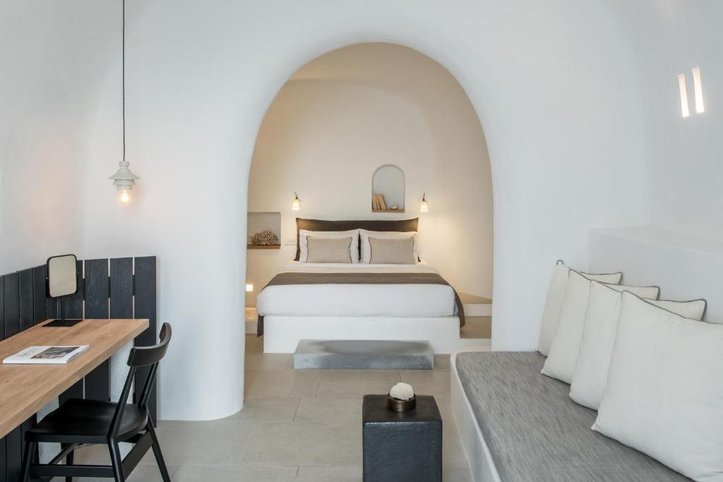 Mūsdienīgs un elegants guļamistabas interjers ar baltām sienām, koka mēbelēm un komfortablu gultu, kas rada relaksējošu atmosfēru. Iekārtota zona ar dīvānu un darba galdu.