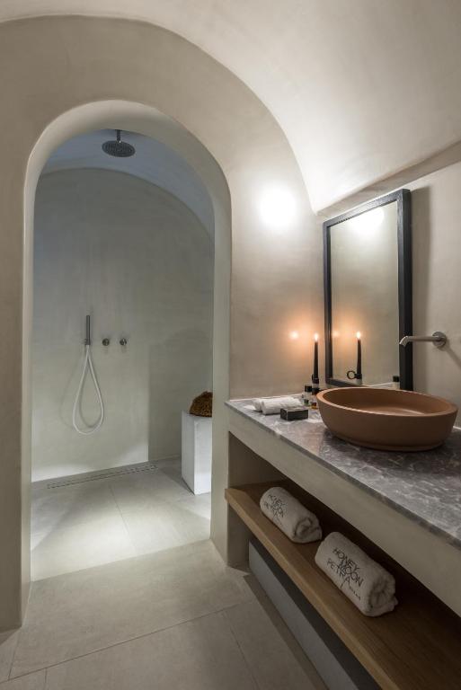 Mūsdienīgs vannas istabas interjers ar arku, dušu un minimālisma dizainu. Uz galda ir gluda marmora virsma un keramikas izlietne, apgaismojums rada patīkamu atmosfēru.