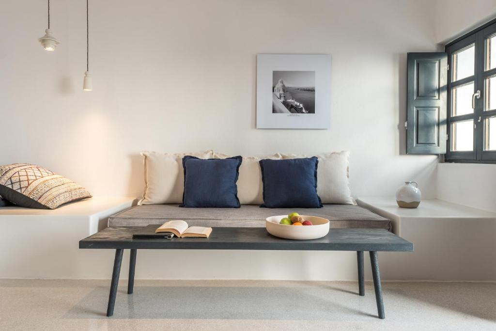 Mūsdienīgs dzīvojamās istabas interjers ar pelēku dīvānu, zilu spilvenu un koka galdu, uz kura atrodas grāmata un augļu trauks. Logi ar zaļām aizvērtām žalūzijām un minimālistiskais apgaismojums rada mājīgu atmosfēru.