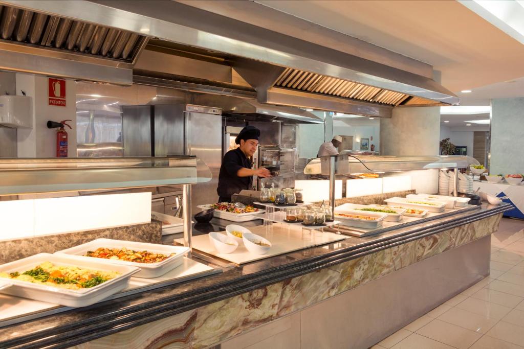 Virtuves skats ar šefpavāru, kas gatavo ēdienus un piedāvā dažādus ēdienus. Uz galda ir pasniegti zaļumi un dārzeņi.