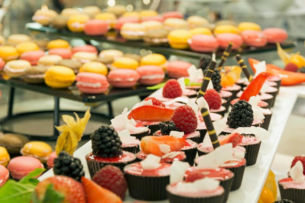 Saldumu bufete ar krāsainiem makaronu un augļu desertiem, kas rotāti ar ogām un šokolādes strīpiņām.