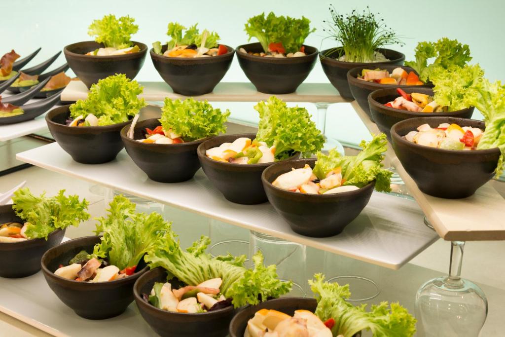 Eleganti izkārtoti melni trauki ar svaigiem dārzeņiem un salātu lapām, pasniegti stilīgā uzstādījumā. Ideāla izvēle viesību galda noformēšanai.