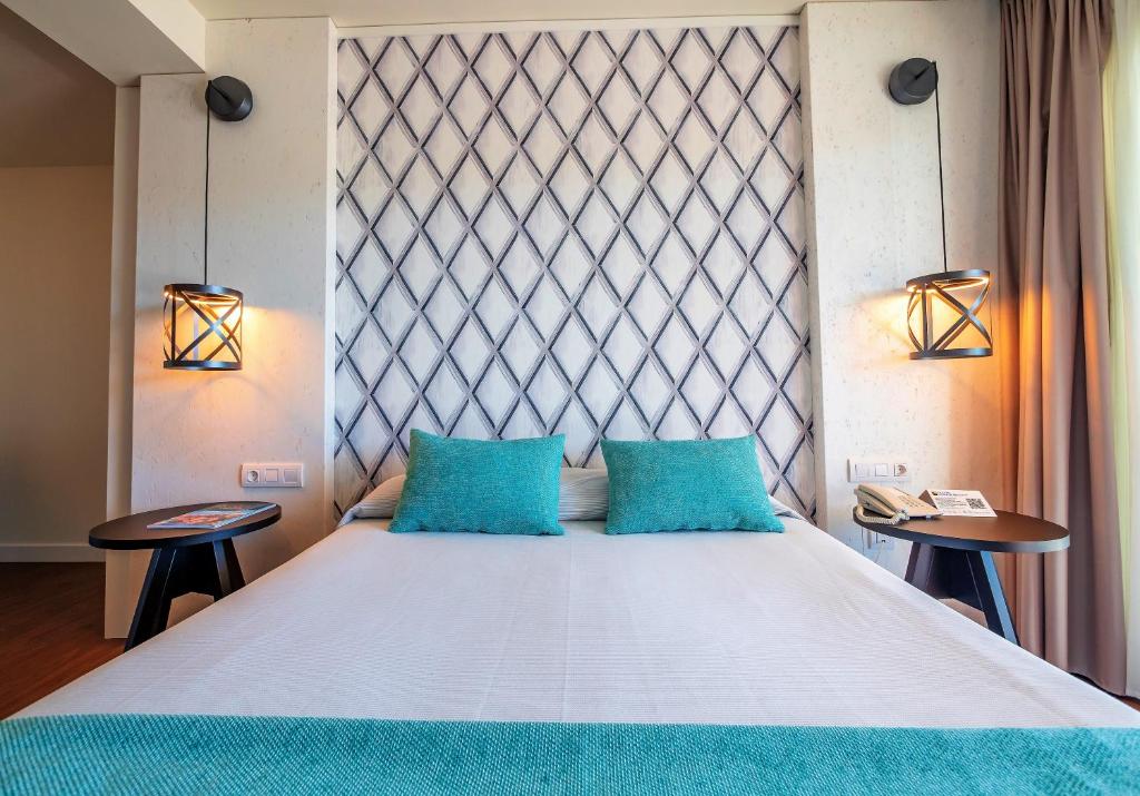 Mūsdienīgs guļamistabas interjers ar gultu un dekoratīvām spilvenēm, kas izceļas ar zilu tonusu. Sienas apgaismotas ar stilīgām lampām, radot patīkamu atmosfēru.