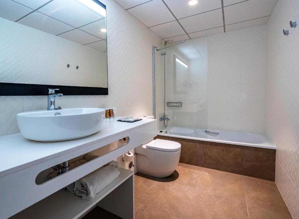 Mūsdienīgs vannas istabas interjers ar baltu izlietni, spoguli un dušas kabīni, kas apvienota ar vannu. Eleganti izkārtota telpa ar dabīgu apgaismojumu un neitrālām krāsām.