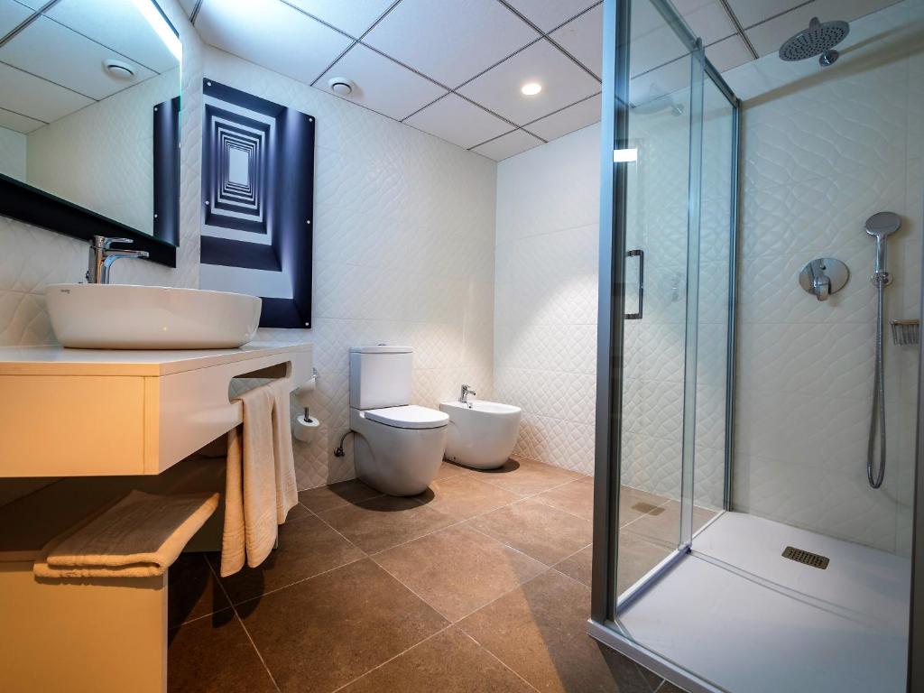 Mūsdienīga vannas istaba ar dušu, tualeti un izlietni, dekorēta ar neitrālām krāsām un modernu apgaismojumu. Vannas istaba ir plaša, ar flīžu grīdu un stilīgu sienu mākslu.