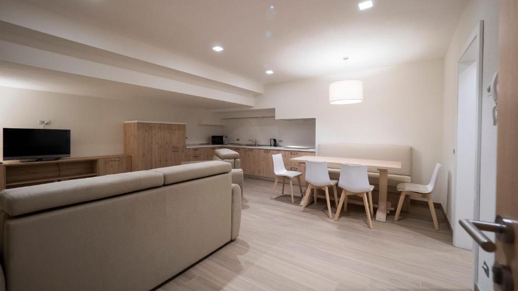 Mūsdienīga viesistaba ar gaišu interjeru, kurā ir dīvāns, televizors un ēdamgalds ar krēsliem. Telpa ir plaša un labi apgaismota, radot patīkamu atmosfēru.