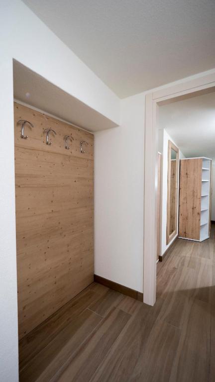 Mūsdienīgs priekšnams ar koka apdari un sienu pakaramiem, kas nodrošina praktisku un estētisku telpas risinājumu. Redzama arī spoguļa un plauktu sistēma, kas papildina interjeru.